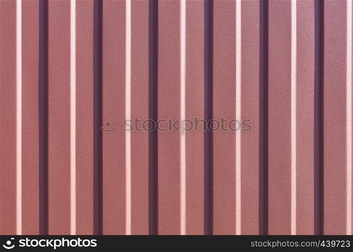 Brown metallic fence made of corrugated steel sheet with vertical guides. Corrugated brown iron sheet background close up.. Brown corrugated steel sheet with vertical guides.
