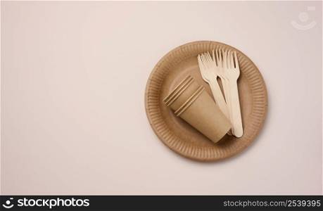 Brown paper cups and plates on a beige background. Recyclable garbage, rejection of plastic, top view
