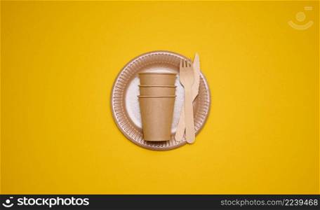 brown paper cups and plates on a yellow background. Recyclable garbage, rejection of plastic, top view