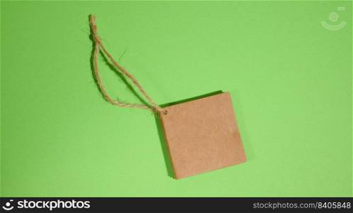 Brown paper square paper tag with rope on green background, top view 
