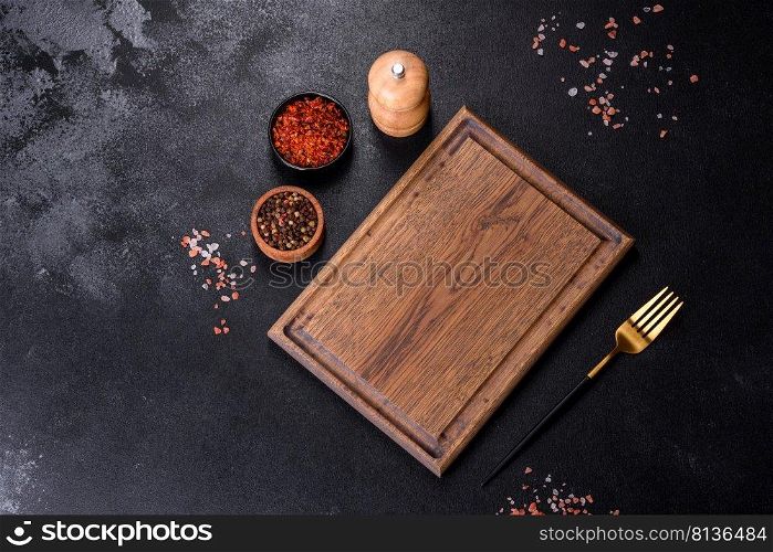 Brown rectangular wooden cutting board with salt and spices on a dark concrete background. Cooking at home. Brown rectangular wooden cutting board with salt and spices on a dark concrete background