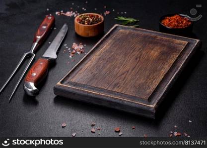 Brown rectangular wooden cutting board with salt and spices on a dark concrete background. Cooking at home. Brown rectangular wooden cutting board with salt and spices on a dark concrete background
