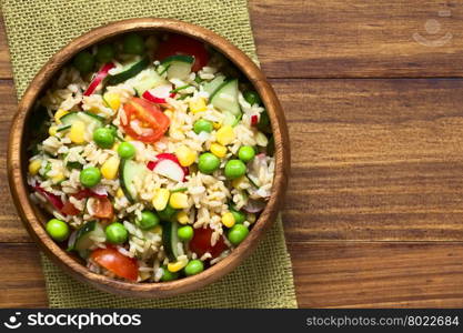 Brown rice salad with cherry tomato, corn, cucumber, radish, pea and chives served in bowl, photographed overhead on dark wood with natural light (Selective Focus, Focus on the top of the salad)