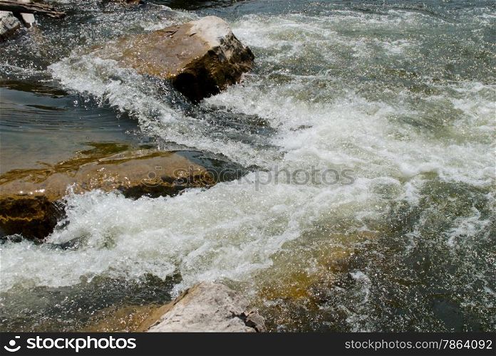 Brown rocks and churning water in clear river.