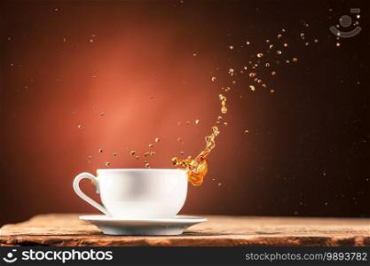 Brown splashes out drink from white cup of tea on a brown wooden background.. Brown splashes out drink from cup of tea on a brown background