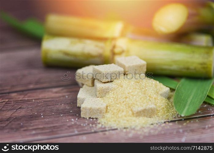 Brown sugar cubes and sugar cane on wooden table and sunlight nature background