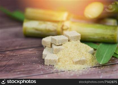 Brown sugar cubes and sugar cane on wooden table and sunlight nature background