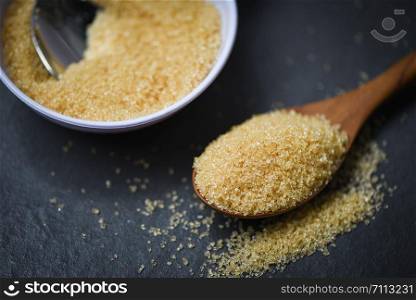 brown sugar in wooden spoon on dark black background with cane sugar on white bowl , close up