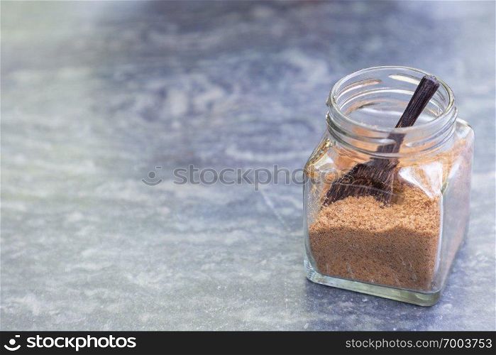 Brown sugar with wooden spoon in glass bottle on gray stone table in coffee shop.