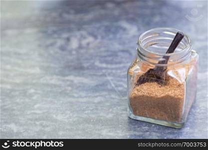 Brown sugar with wooden spoon in glass bottle on gray stone table in coffee shop.