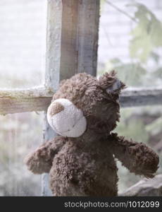 brown teddy bear sits on a windowsill and looks out the window, nostalgia concept