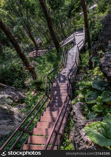 Brown wooden staircase with metal railings and surrounding green trees on mountain path. No focus, specifically.