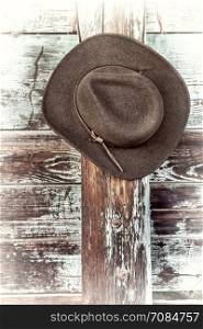 brown wool felt cowboy hat with leather headband hanging on weathered wooden corral fence, retro hand tinted processing