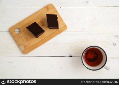 brownie cake on a bamboo tray with cuo of tea on a white wooden background with space for textt. top view
