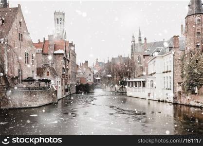 Bruges, Belgium canals view in winter snowfall. Stunning fairy landscape with historical buildings and calm icy water. Christmas mood. Monochromatic neutral tones with natural light