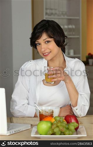 brunette all smiles sitting at table with laptop having breakfast
