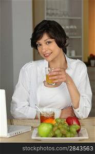 brunette all smiles sitting at table with laptop having breakfast