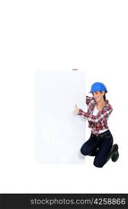 Brunette builder giving thumbs-up by blank poster