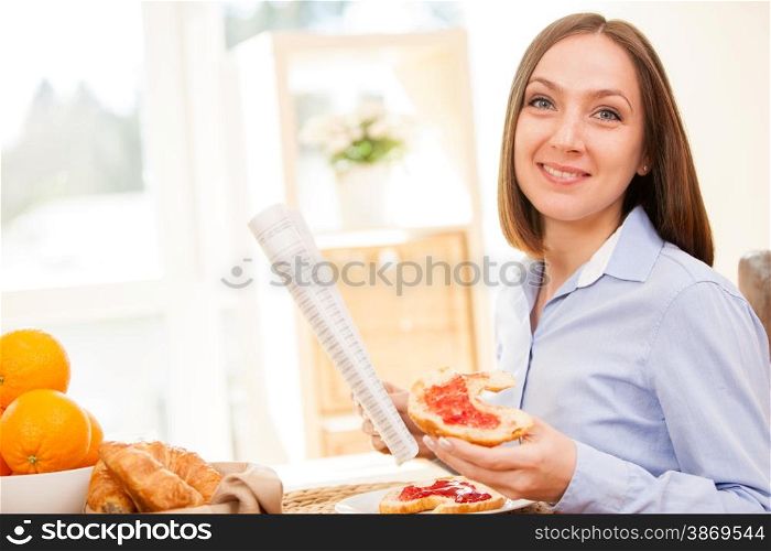 Brunette businesswoman is reading the newspaper while having breakfast at home