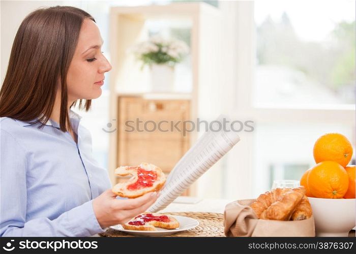 Brunette businesswoman is reading the newspaper while having breakfast at home