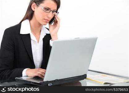 Brunette businesswoman using laptop and mobile telephone