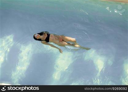 Brunette caucasian woman in  bikini floating in the pool water
