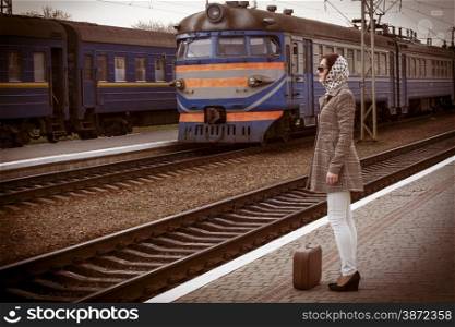 Brunette caucasian woman with glasses and coat waiting at the railway station with a suitcase