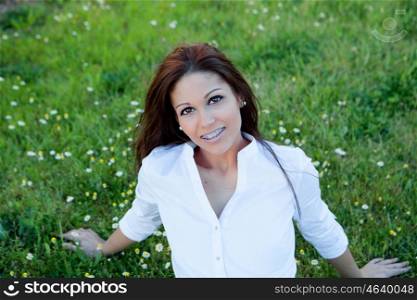 Brunette cool girl with brackets sitting on the grass with many daisies