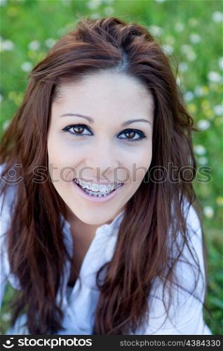 Brunette cool girl with brackets sitting on the grass with many flowers