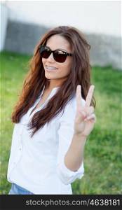 Brunette cool girl with sunglasses in the park gesturing the victory signal