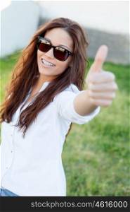Brunette cool girl with sunglasses in the park saying OK