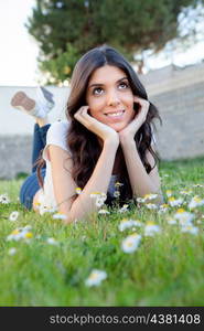 Brunette girl lying on the grass with many daisies around thinking