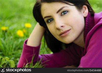 Brunette girl take pleasure on the grass with dandelions, outdoor portrait. Close up face