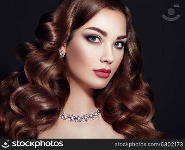 Brunette Girl with Long and shiny Curly Hair. Beautiful Model Woman with Curly Hairstyle. Care and Beauty Hair products. Perfect Make-Up and Jewelry