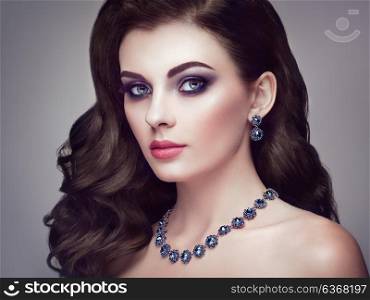 Brunette Girl with Long and shiny Curly Hair. Beautiful Model Woman with Curly Hairstyle. Care and Beauty Hair products. Perfect Make-Up and Jewelry