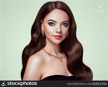 Brunette Girl with Long Healthy and Shiny Curly Hair. Care and Beauty. Beautiful Model Woman with Wavy Hairstyle. Make-Up and Jewelry
