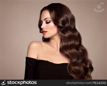 Brunette Girl with Long Healthy and Shiny Curly Hair. Care and Beauty. Beautiful Model Woman with Wavy Hairstyle. Make-Up and Black Dress