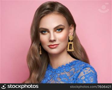 Brunette girl with perfect makeup. Beautiful model woman with curly hairstyle. Care and beauty hair products. Lady with fashionable gold makeup. Model with jewelry on pink background