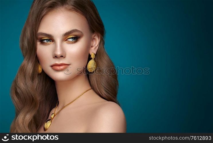 Brunette girl with perfect makeup. Beautiful model woman with curly hairstyle. Care and beauty hair products. Lady with fashionable gold makeup. Model with jewelry on dark blue background