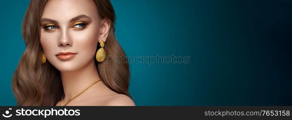 Brunette girl with perfect makeup. Beautiful model woman with curly hairstyle. Care and beauty hair products. Lady with fashionable gold makeup. Model with jewelry on dark blue background
