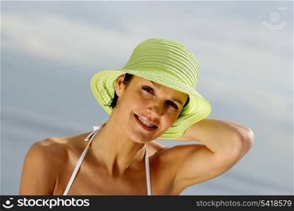 Brunette holding on to her hat at the beach