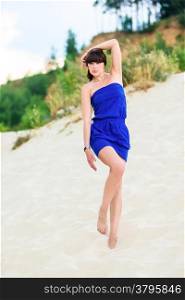 brunette in a blue dress on the beach sand