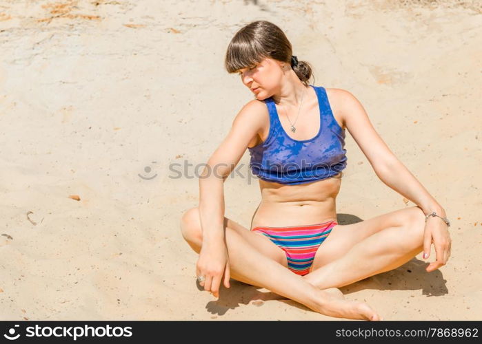 brunette in a blue shirt relaxing in lotus pose on the beach