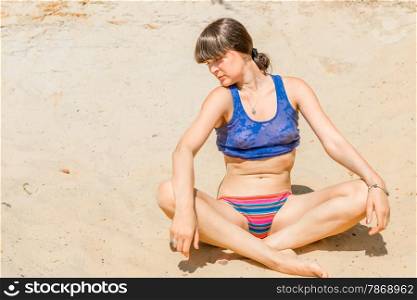 brunette in a blue shirt relaxing in lotus pose on the beach