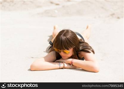 Brunette in bathing suit basking in the hot sand on the beach