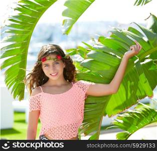 Brunette kid girl at banana tree leaves in bright day light in Mediterranean