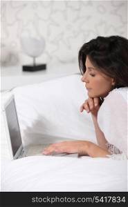 Brunette laying in bed with laptop computer