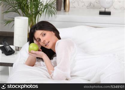 Brunette laying on bed holding apple
