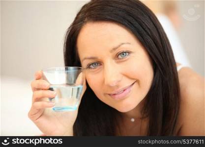 Brunette laying on bed with glass of water