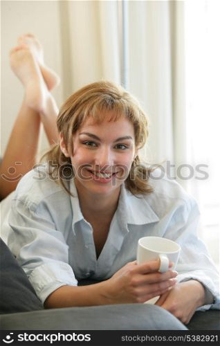 Brunette laying on sofa with mug of coffee
